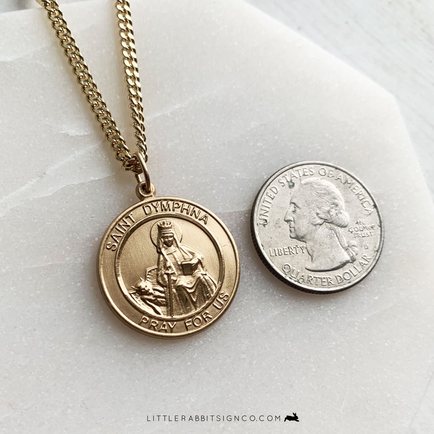 Saint Dymphna Pray For Us is on a Gold Men's Round Medal next to a quarter for a size comparison. Men's mental health is so important. Saint Dymphna is the patron saint of mental health, anxiety, and depression.