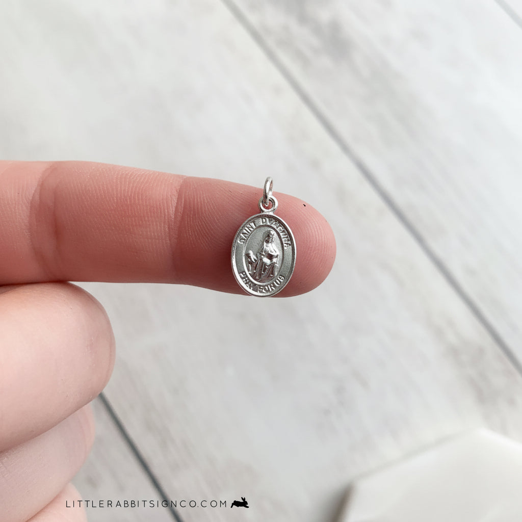 Tiny Saint Dymphna sterling silver medal shown on fingertip for size reference — petite Catholic patron saint medal handmade in the USA