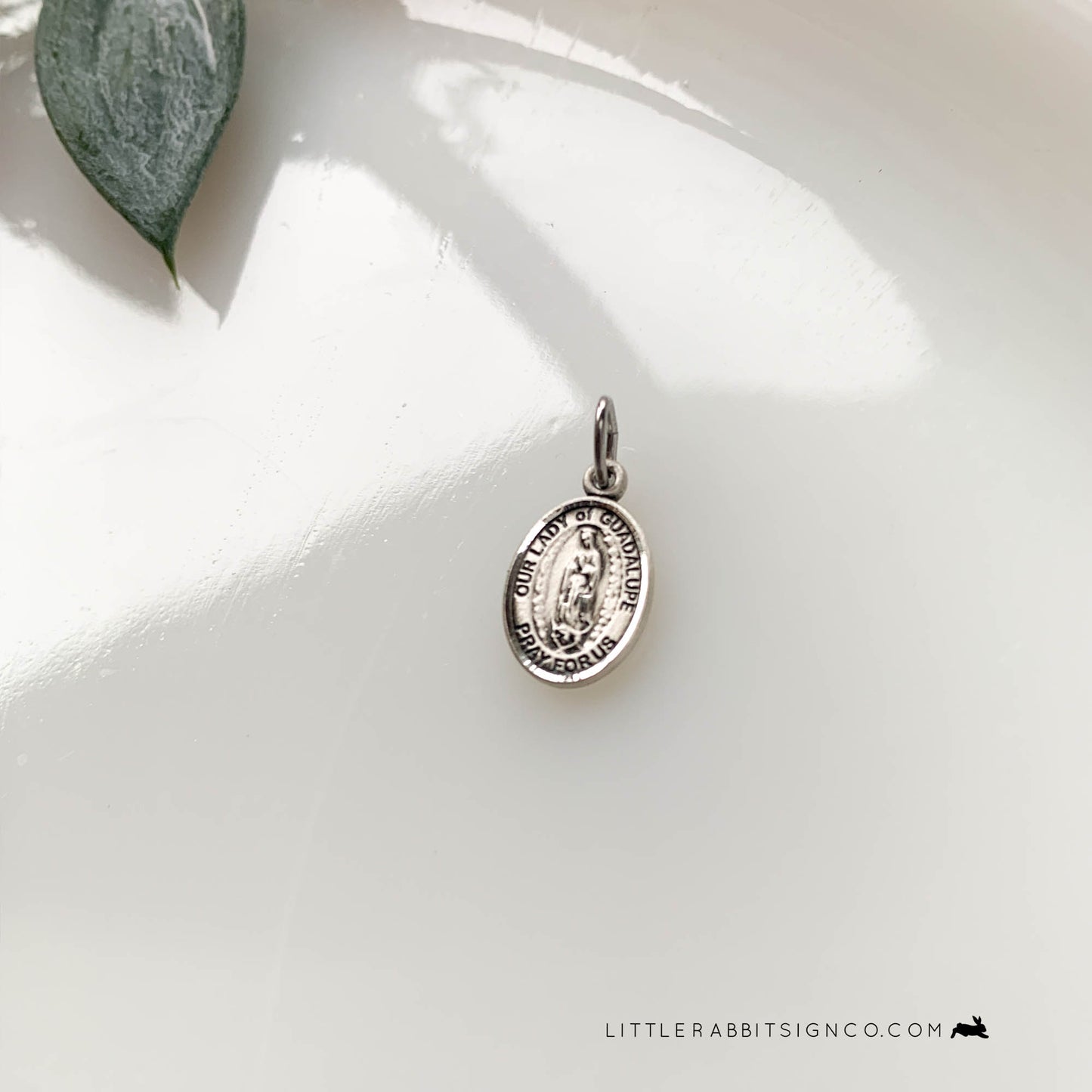 Our Lady of Guadalupe Medal in sterling silver on a white stone background. This tiny medal is 1/2 inch tall by 1/4 inch wide. It is the perfect medal charm to add to your necklace or sacramentals. Attach it to your favorite rosary and enjoy the devotion of Our Lady of Guadalupe.