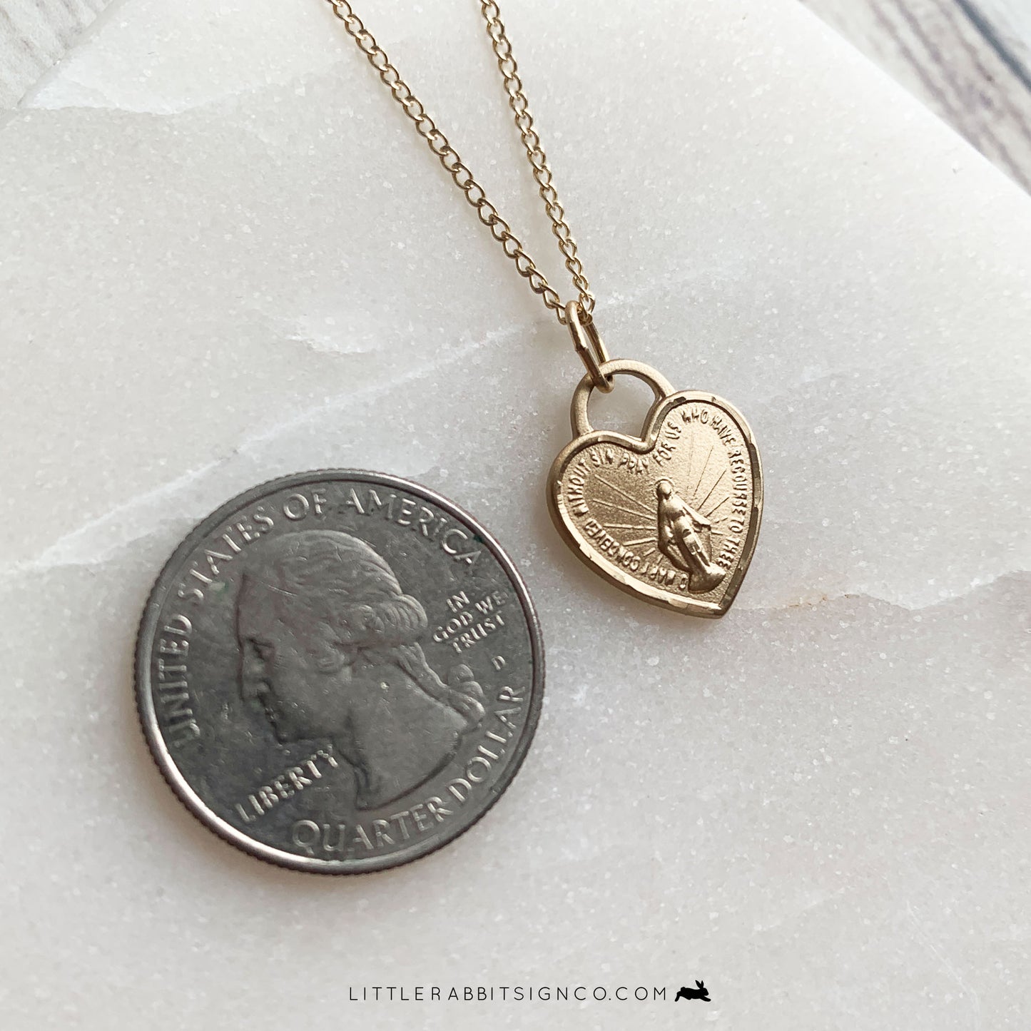 Size reference of the Gold Miraculous Medal Heart Shaped necklace next to a Quarter.