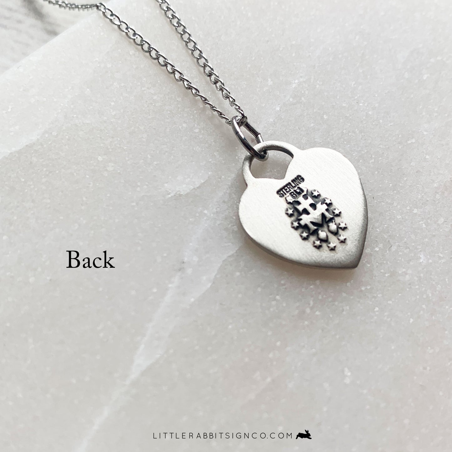 Back of the heart-shaped Miraculous Medal necklace in sterling silver. Shows the traditional Miraculous Medal pendant back.