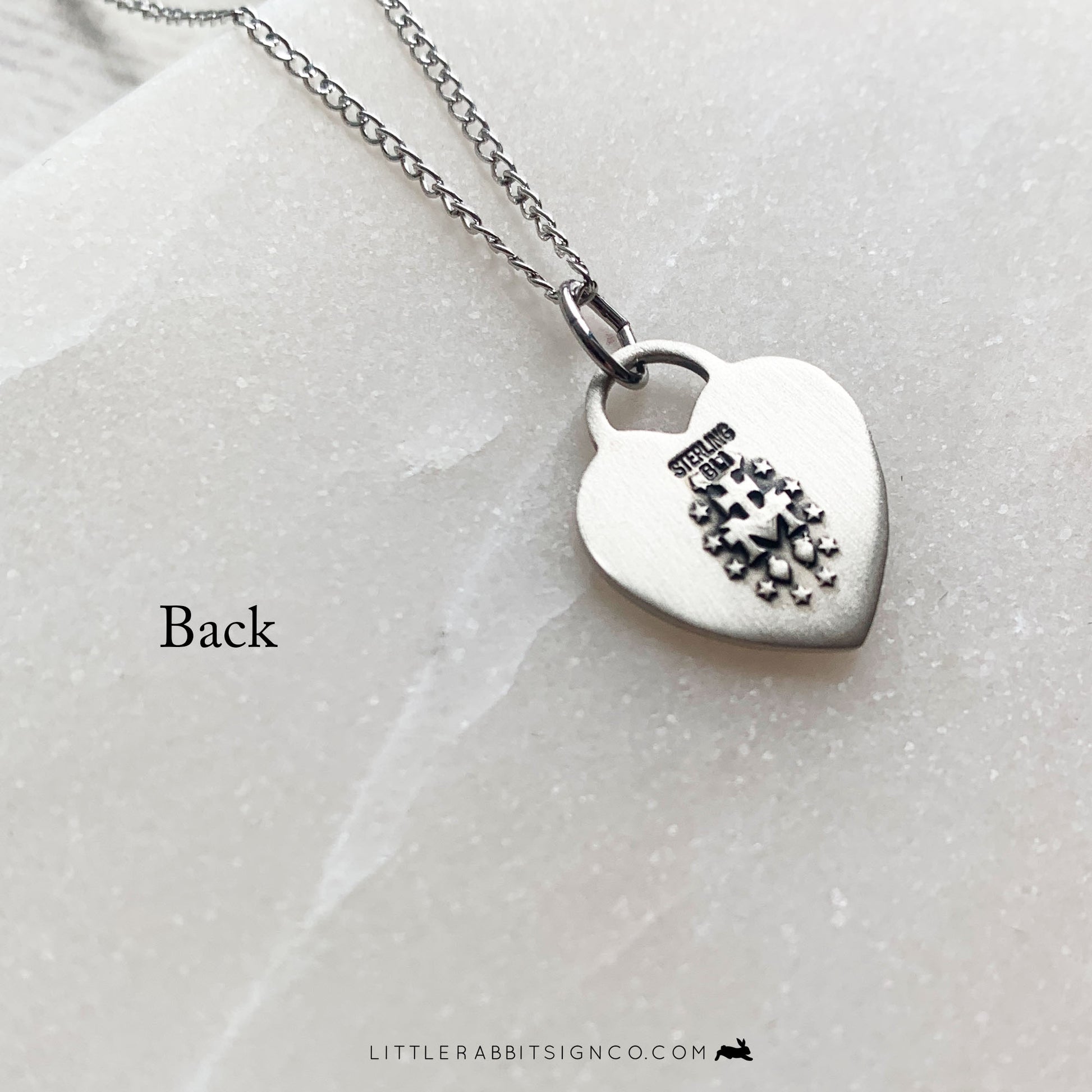Back of the heart-shaped Miraculous Medal necklace in sterling silver. Shows the traditional Miraculous Medal pendant back.