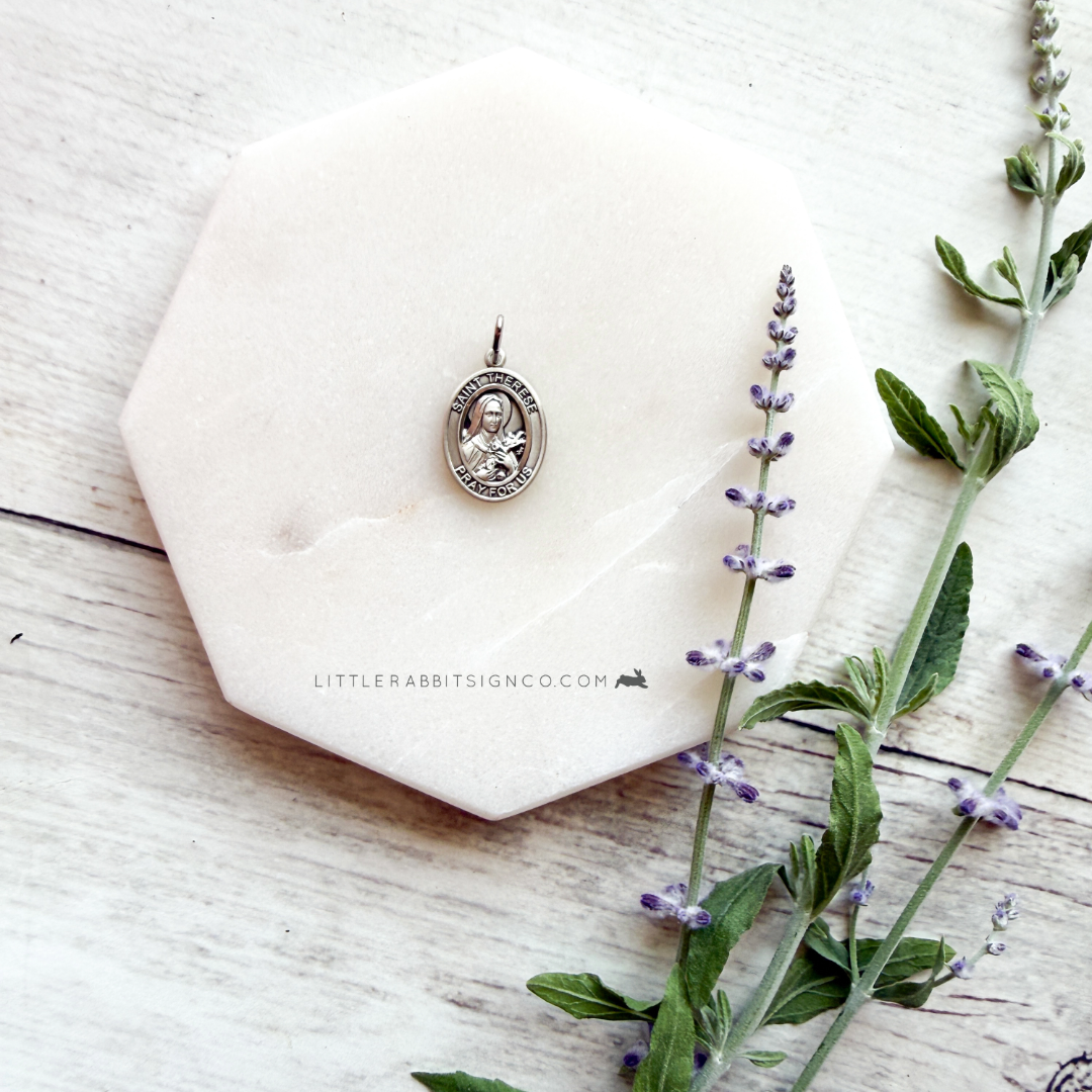 Sterling silver Saint Thérèse of Lisieux medal pendant on white fabric with lavender flowers — heirloom Catholic jewelry