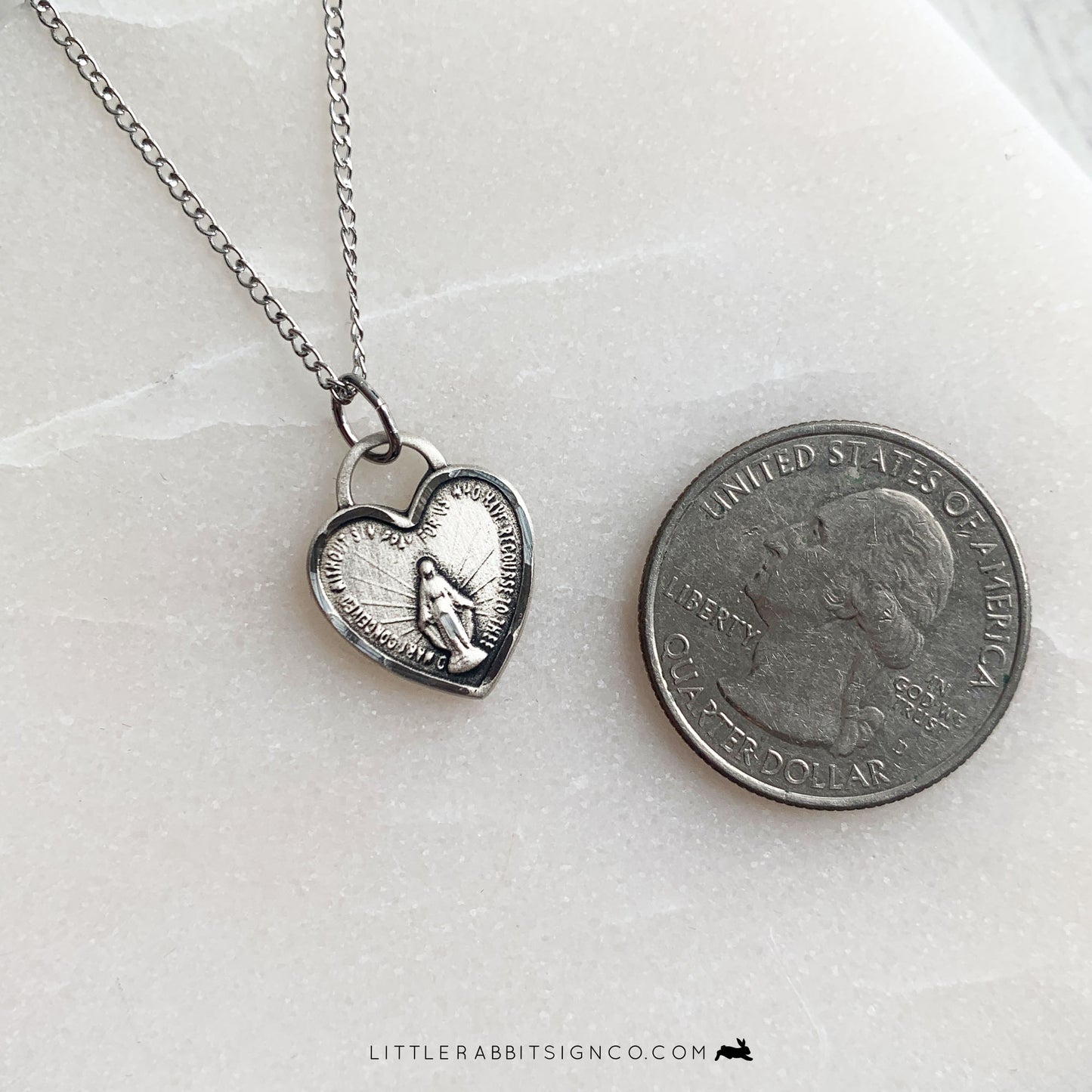 This Sterling Silver Miraculous Medal heart shaped necklace is shown next to a quarter for size reference.